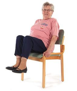 Tuolilla istuva jumppaaja on nostanut molemmat polvet ylös koukkuun irti lattiasta ja pitää käsillä kiinni tuolin reunoista.
