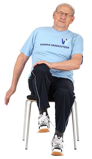 Tuolilla istuva jumppaaja on nostanut oikean polven ylös ja koskettaa vasemmalla kädellä oikeaa polvea. Vasen jalkapohja on kiinni lattiassa ja oikea käsi roikkuu suorana vartalon sivulla.