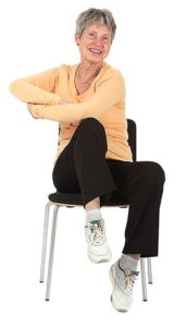 Tuolilla istuva jumppaaja on nostanut oikean polven ylös ja koskettaa vasemmalla kyynärpäällä oikeaa polvea.
