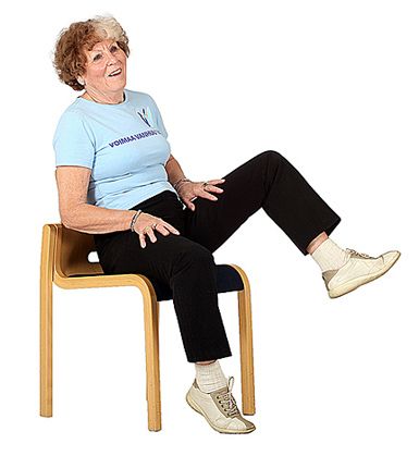 Jumppaaja istuu tuolilla ja on viemässä vasenta polvea sivulle painon ollessa oikealla kankulla.