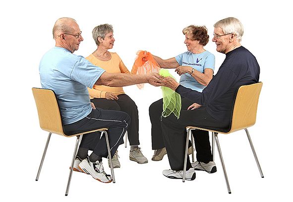 Neljä jumppaajaa istuu tuoleilla piirissä ja kierrättää kahta huivia samaan suuntaan. Kaksi jumppaajista on antamassa toisella kädellä huiveja vierustoverillensa